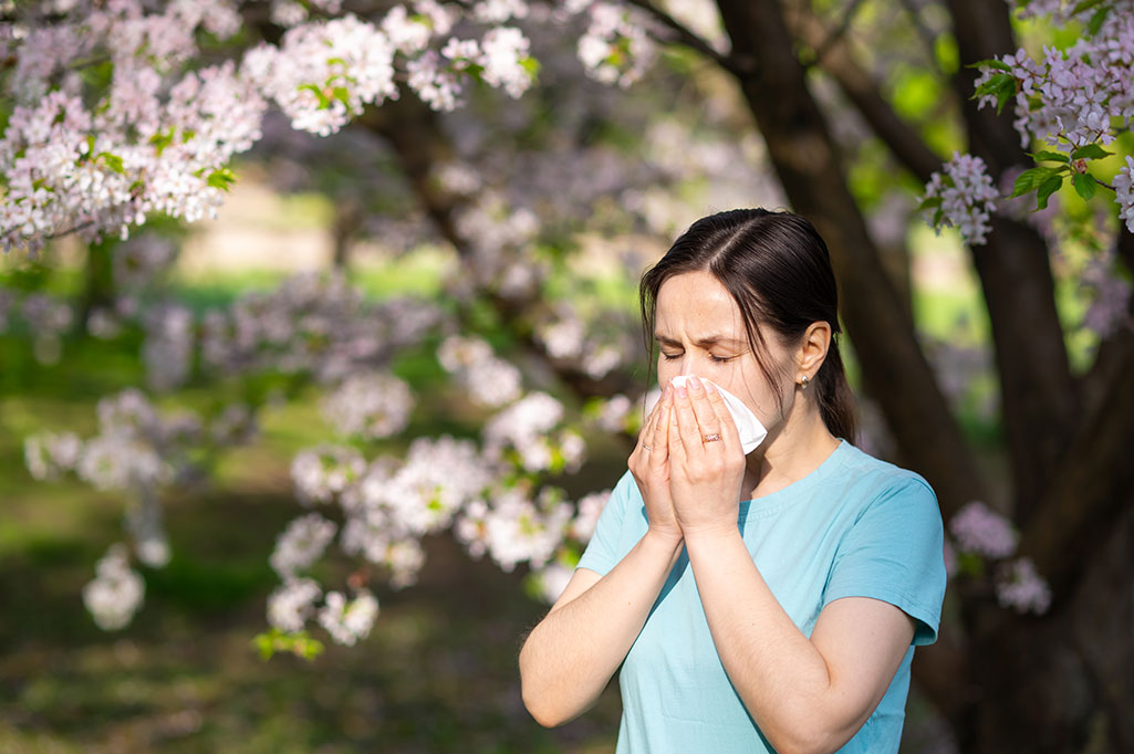 woman-sneezing-into-tissue-in-blooming-garden
